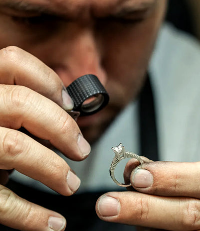 Person examining a diamond ring with a magnifying glass