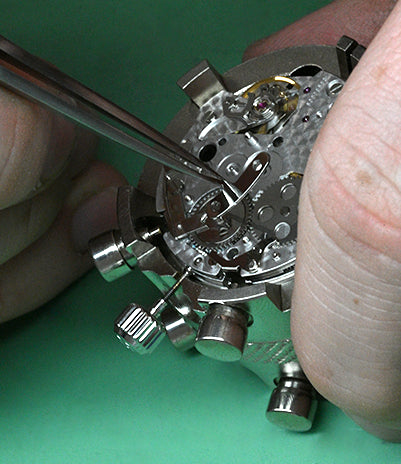 Watch mechanism being adjusted with a tool on a green background