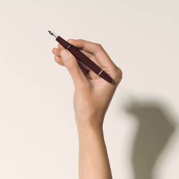 Hand holding a brown fountain pen against a beige background